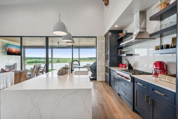 Modern kitchen with white island, dark cabinets, stainless appliances, pendant lights, and large windows with scenic views.