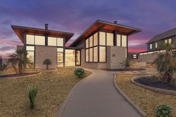 A modern house with large windows, contemporary design, desert landscaping, and a curved walkway under a vibrant purple sky.