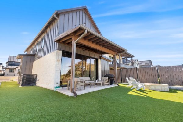 A modern house with a patio, outdoor furniture, and artificial grass in the backyard under a clear blue sky.