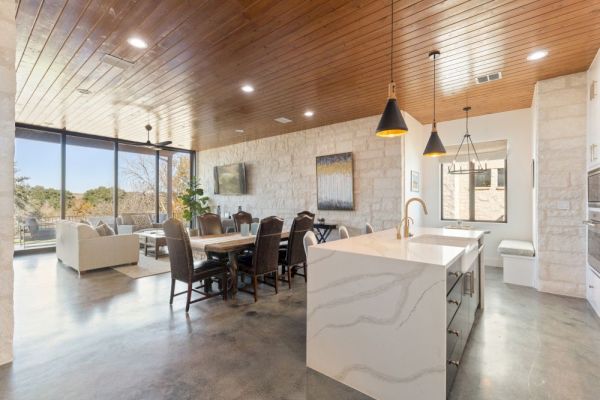 Open-concept living area with a kitchen island, dining table, and seating area. Large windows provide plenty of natural light.