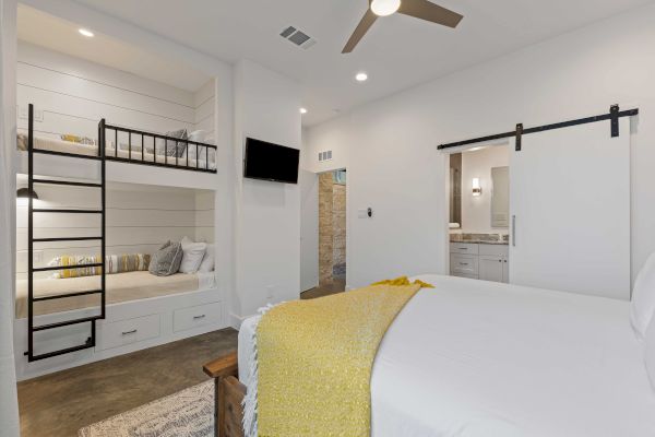 A modern bedroom with a bed, bunk beds, a yellow blanket, a TV, and a sliding door to a bathroom.